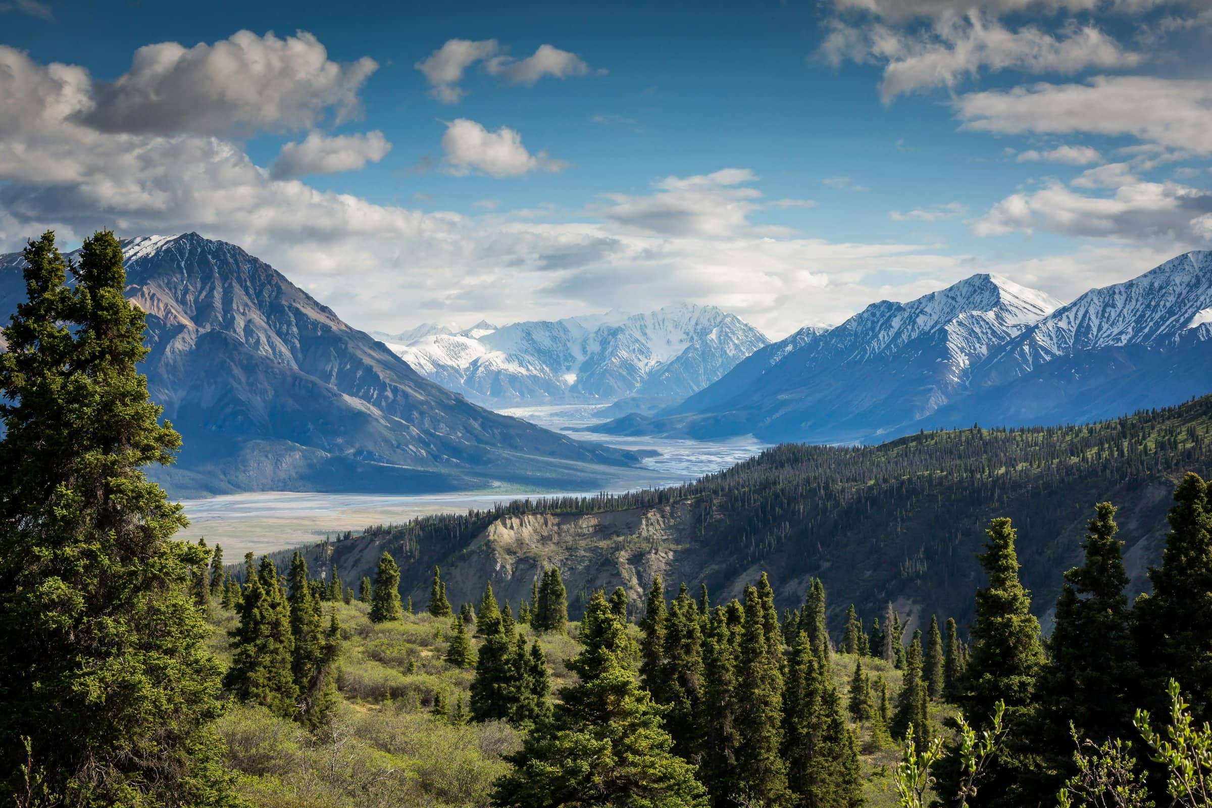 A wide braided valley below snow-capped mountains